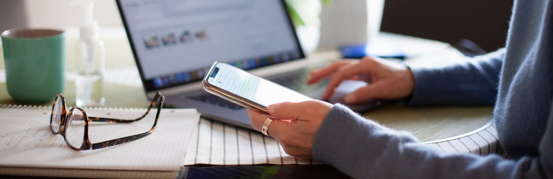 A woman sits at her desk and scrolls through her phone.