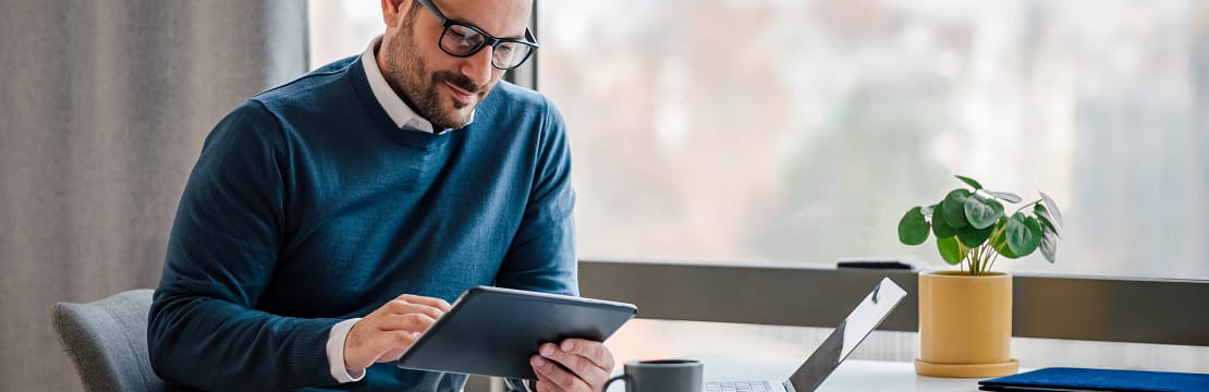 Man with glasses reading his tablet in an office.